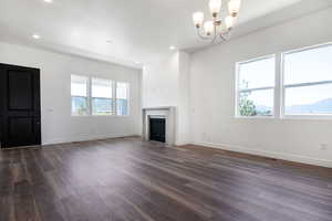 Unfurnished living room featuring a notable chandelier, plenty of natural light, and dark hardwood / wood-style floors