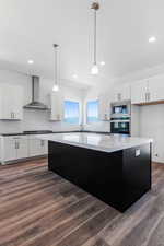 Kitchen featuring stainless steel appliances, white cabinets, wall chimney exhaust hood, and pendant lighting