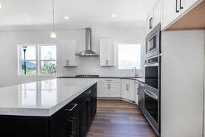 Kitchen featuring sink, wall chimney exhaust hood, pendant lighting, a kitchen island, and appliances with stainless steel finishes