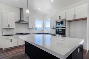 Kitchen featuring white cabinetry, pendant lighting, wall chimney range hood, and appliances with stainless steel finishes