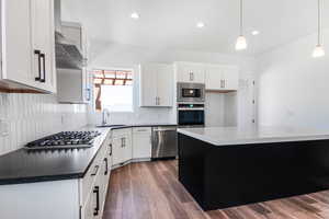 Kitchen with stainless steel appliances, sink, decorative light fixtures, white cabinets, and a center island