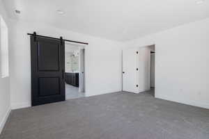 Unfurnished bedroom with a barn door, light carpet, and ensuite bath