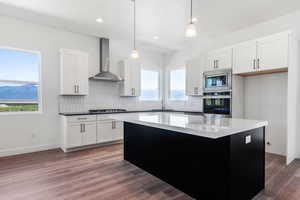 Kitchen featuring white cabinets, wall chimney range hood, sink, appliances with stainless steel finishes, and decorative light fixtures