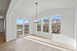 Unfurnished dining area with a notable chandelier, vaulted ceiling, and light hardwood / wood-style flooring