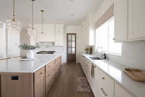 Kitchen featuring dark wood-type flooring, sink, decorative light fixtures, white cabinetry, and a large island