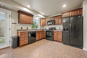 Kitchen with black appliances, light tile patterned flooring, light stone countertops, and sink