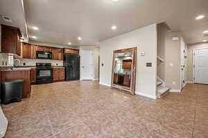 Kitchen with light tile patterned floors, sink, light stone counters, and black appliances