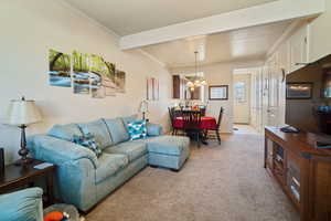 Living room featuring light carpet, a textured ceiling, crown molding, beam ceiling, and a notable chandelier