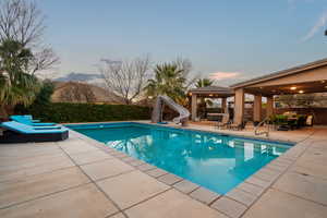 Pool at dusk featuring a water slide and a patio