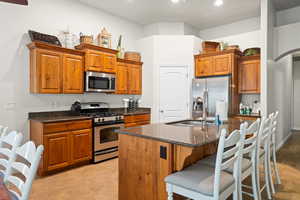 Kitchen with sink, stainless steel appliances, dark stone countertops, a breakfast bar, and a center island with sink