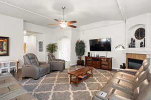 Living room featuring ceiling fan, a fireplace, dark wood-type flooring, and vaulted ceiling