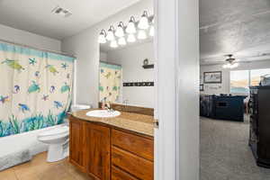 Full bathroom with ceiling fan, shower / bath combination with curtain, a textured ceiling, toilet, and vanity