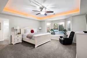 Carpeted bedroom featuring ceiling fan and a tray ceiling