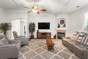 Living room with ceiling fan, lofted ceiling, and a tiled fireplace