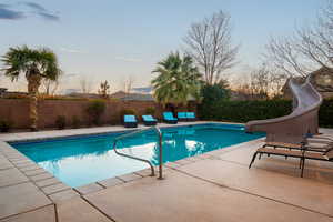 Pool at dusk featuring a patio area and a water slide