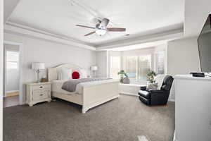 Carpeted bedroom featuring a tray ceiling and ceiling fan