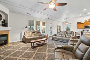 Living room with rail lighting, ceiling fan, a tile fireplace, hardwood / wood-style flooring, and lofted ceiling