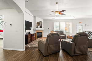 Living room with ceiling fan, a fireplace, and dark wood-type flooring