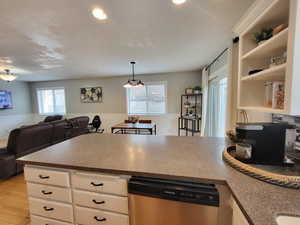 Kitchen with a notable chandelier, white cabinets, stainless steel dishwasher, light wood flooring, and decorative light fixtures