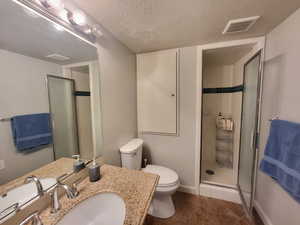 Bathroom featuring vanity, a shower with door, tile patterned flooring, toilet, and a textured ceiling