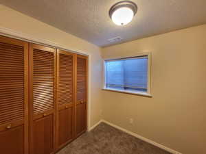 Office with a textured ceiling, dark carpet, and a closet