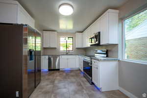 Kitchen with white cabinets, appliances with stainless steel finishes, a healthy amount of sunlight, and sink