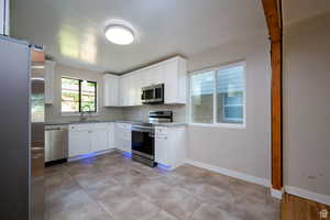 Kitchen with light stone counters, sink, white cabinets, and appliances with stainless steel finishes