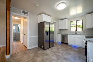 Kitchen with light stone counters, sink, white cabinets, and appliances with stainless steel finishes