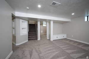 Basement featuring light carpet, built in shelves, and a textured ceiling