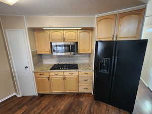 Kitchen featuring decorative backsplash, light stone countertops, dark wood-type flooring, black appliances, and light brown cabinets