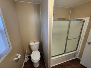 Bathroom with wood-type flooring, combined bath / shower with glass door, and toilet