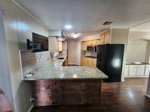 Kitchen with black appliances, light stone counters, kitchen peninsula, and sink