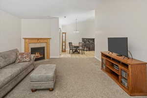 Carpeted living room featuring a notable chandelier, lofted ceiling, and a tiled fireplace