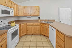 Kitchen featuring kitchen peninsula, light brown cabinetry, white appliances, sink, and light tile patterned flooring