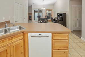 Kitchen with dishwasher, light brown cabinets, sink, pendant lighting, and light tile patterned floors