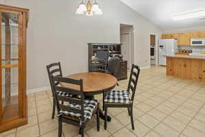 Tiled dining space featuring a chandelier, washer / dryer, and vaulted ceiling