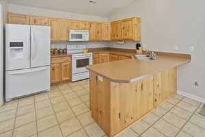 Kitchen with white appliances, sink, vaulted ceiling, light tile patterned flooring, and kitchen peninsula