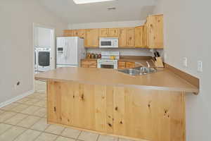 Kitchen featuring kitchen peninsula, light brown cabinets, white appliances, and sink