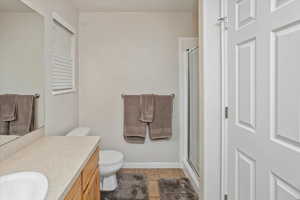 Bathroom with toilet, vanity, tile patterned floors, and an enclosed shower