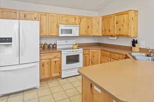 Kitchen featuring sink, vaulted ceiling, white appliances, light brown cabinetry, and light tile patterned floors