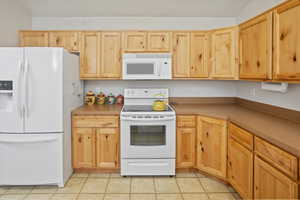 Kitchen with light brown cabinets, light tile patterned flooring, and white appliances