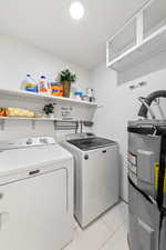 Laundry room featuring electric water heater, washer and clothes dryer, and light tile patterned floors