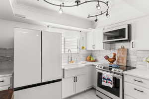 Kitchen featuring stainless steel electric range, backsplash, white refrigerator, sink, and white cabinetry