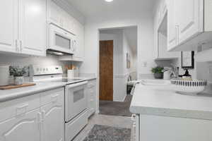 Kitchen featuring light tile, sink, white cabinets, and white appliances