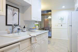 Kitchen featuring ornamental molding, white appliances, sink, light tile patterned floors, and white cabinetry