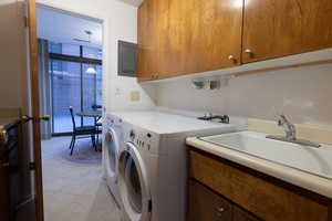 Washroom featuring washer and clothes dryer, cabinets, electric panel, sink, and light tile patterned floors