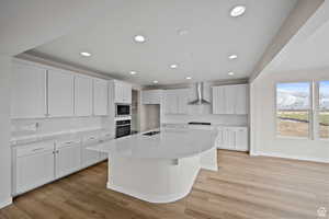 Kitchen with built in microwave, wall chimney range hood, a center island with sink, white cabinets, and oven