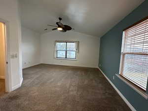 Carpeted spare room featuring vaulted ceiling and ceiling fan