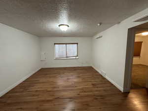 Unfurnished room with a textured ceiling and dark hardwood / wood-style floors