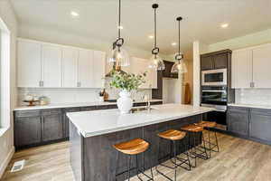 Kitchen featuring white cabinetry, light hardwood / wood-style flooring, decorative backsplash, a center island with sink, and appliances with stainless steel finishes